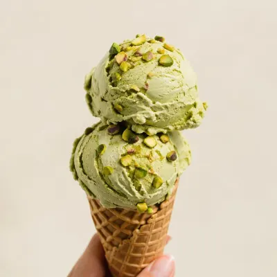 Hoorntje met twee bolletjes pistache-ijs bestrooid met gehakte pistachenoten